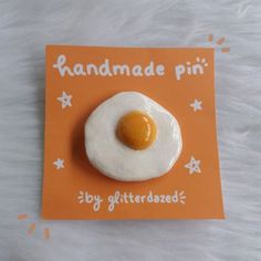 an orange card with a fried egg on it and the words handmade pin written in white