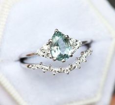 a ring with an aqua blue stone surrounded by white diamonds on top of a cloth