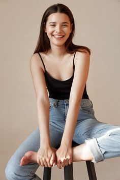 a young woman sitting on top of a stool with her legs crossed and smiling at the camera