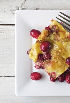 a white plate topped with fruit covered in sauce and cranberries next to a fork