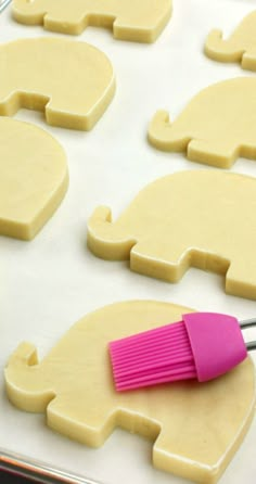 a pink brush sitting on top of a pan filled with cut out elephant shaped cookies