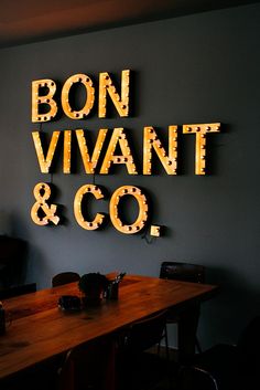 a wooden table sitting in front of a neon sign that says bonn vivant and co