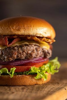 a hamburger with bacon, lettuce and tomato on it sitting on a cutting board