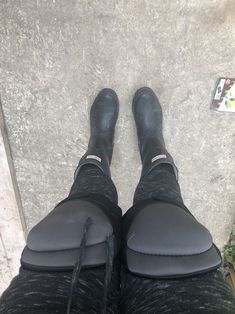 the legs and feet of a person wearing black shoes, standing on concrete with their boots up