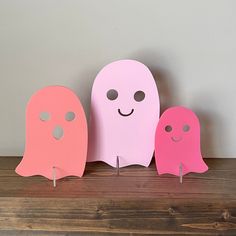 three pink and one pink ghost standing next to each other on top of a wooden table