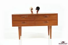 two small figurines are sitting on top of a wooden dresser with drawers and legs