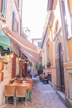 an alleyway with tables and umbrellas on both sides, surrounded by stone buildings