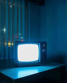 an old tv sitting on top of a wooden table in front of a curtained window