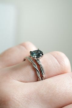 a woman's hand holding an engagement ring with a green stone in it and two twisted bands