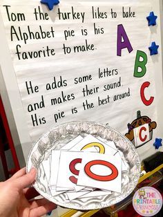 a person holding up a paper plate with letters and numbers on it in front of a bulletin board