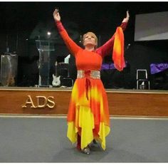 a woman in an orange and yellow dress with her arms up while standing on a stage