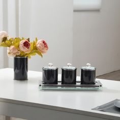 three black canisters with flowers in them sitting on a white countertop next to a silver tray