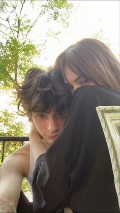 two young women embracing each other in front of trees