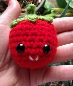 a hand holding a small red crocheted strawberry ornament with black eyes