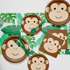 paper plates with monkey faces on them and green palm leaves around the edges, along with forks and napkins