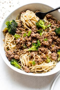 a white bowl filled with meat and broccoli on top of a table next to a fork