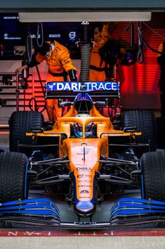 an orange and blue race car is parked in front of a building with workers working on it