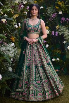 a woman standing in front of flowers wearing a green and pink lehenga