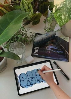 a person is using an ipad to draw graffiti on the table next to potted plants