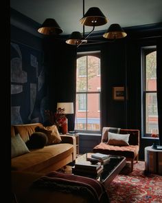 a living room filled with furniture and two lamps hanging from the ceiling next to windows