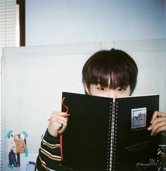 a young boy holding up a book in front of his face