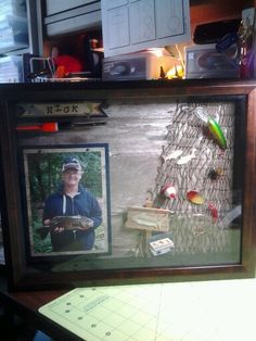 a man holding a fish in his hand next to a wooden frame with pictures on it