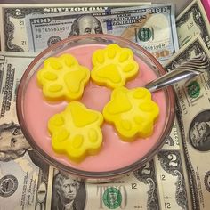 four yellow dog paw shaped treats in a bowl on top of money with a spoon