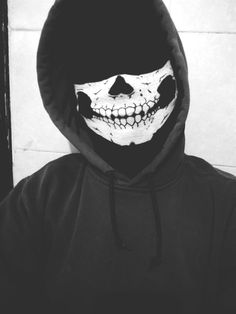 a person wearing a skeleton mask and black hoodie in front of a white wall