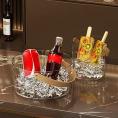 two wine bottles and ice buckets sitting on a counter top with glasses in it