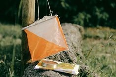 an orange and white kite hanging from a wooden pole in the grass next to a rock