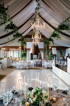 a banquet hall with tables and chairs covered in white draping, chandeliers and greenery