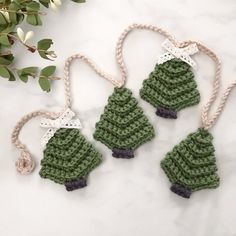 three crocheted christmas tree ornaments hanging from twine on a marble counter top