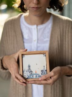 a woman holding a small box with a painting on it's front and side