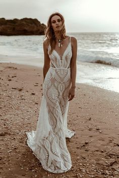 a woman standing on top of a beach next to the ocean wearing a white dress