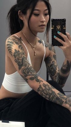 a woman with tattoos is taking a selfie in front of her mirror while sitting on the floor