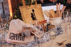 the table is set with wine glasses, utensils and an old - fashioned sign