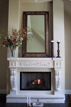 a fireplace with a mirror above it and flowers in vases on the mantel