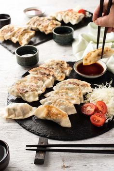 someone is dipping sauce on some dumplings with chopsticks in front of them