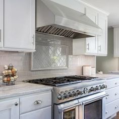 a kitchen with white cabinets and stainless steel stove top oven, range hood and counter tops