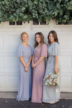 three bridesmaids pose for a photo in front of a garage door with greenery