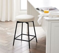 a white counter top sitting under a window next to a bar stool with a cushion on it