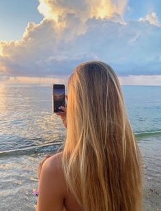 a woman taking a photo of the ocean with her cell phone