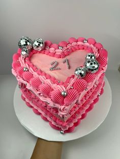 a heart shaped cake with pink icing and silver decorations on the top, sitting on a white plate