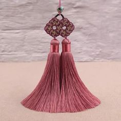 two pink tassels hanging from a hook on a string with beaded decorations