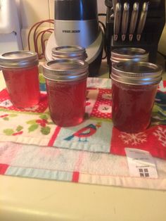 three jars of jam sitting on top of a table next to an electric blender