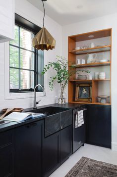 a kitchen with black cabinets and an open book shelf next to the sink in front of a window