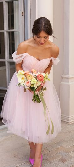 a woman in a pink dress is holding a bouquet and looking down at the ground