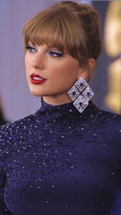 taylor swift at the oscars wearing her hair in a high bun with bangs and blue eyeshadow