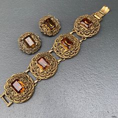 WIDE ~ massive / heavy ~ Vintage ~ Victorian revival ~ gold tone filigree ~ panel bracelet with faceted amber glass cabs ~ Bracelet comes with matching clip-on earrings Unsigned beauty ... Dates mid 20th century Material : gold tone metal amber color glass cabs Measurements : Bracelet is 7 3/4 inches x 1 1/2 inches wide . Earrings are 1 1/4 inches in diameter Condition : Overall all pieces are in good vintage condition with some age related wear ~ can see metal discoloration /darkening ~ Some li Antique Jeweled Metal Jewelry, Jeweled Antique Gold Brass Jewelry, Victorian Style Jeweled Gold Jewelry, Victorian Jeweled Gold Jewelry, Ornate Bronze Jewelry For Formal Occasions, Formal Antique Gold Jewelry With Antique Finish, Formal Antique Gold Jewelry, Ornate Gold Bracelets With Jewels, Vintage Bronze Jeweled Jewelry