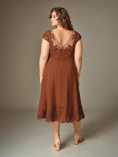 a woman wearing a brown dress with lace detailing on the shoulders and back, standing in front of a gray background